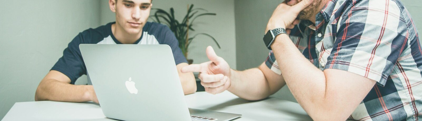 man wearing white and black plaid button-up sports shirt pointing the silver MacBook